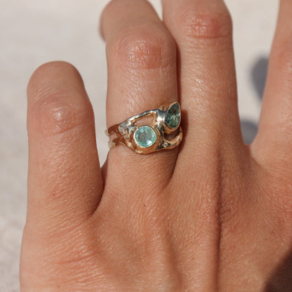 Exquisite ring featuring two vibrant Paraiba tourmalines elegantly bezel-set along a wide, organically shaped band worn on a finger and shown from the side to depict scale and show details.