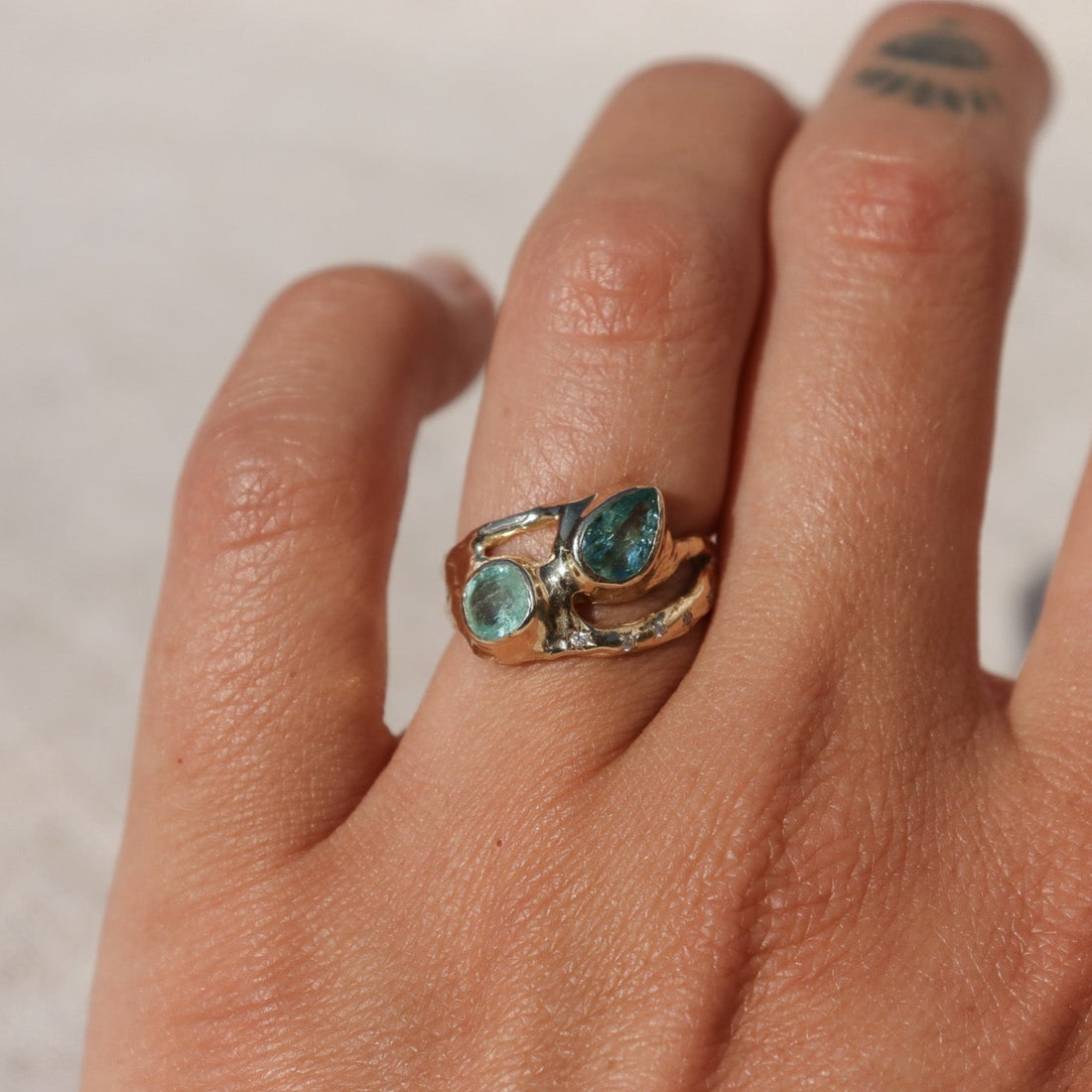 Exquisite ring featuring two vibrant Paraiba tourmalines elegantly bezel-set along a wide, organically shaped band, worn on a finger to depict scale.