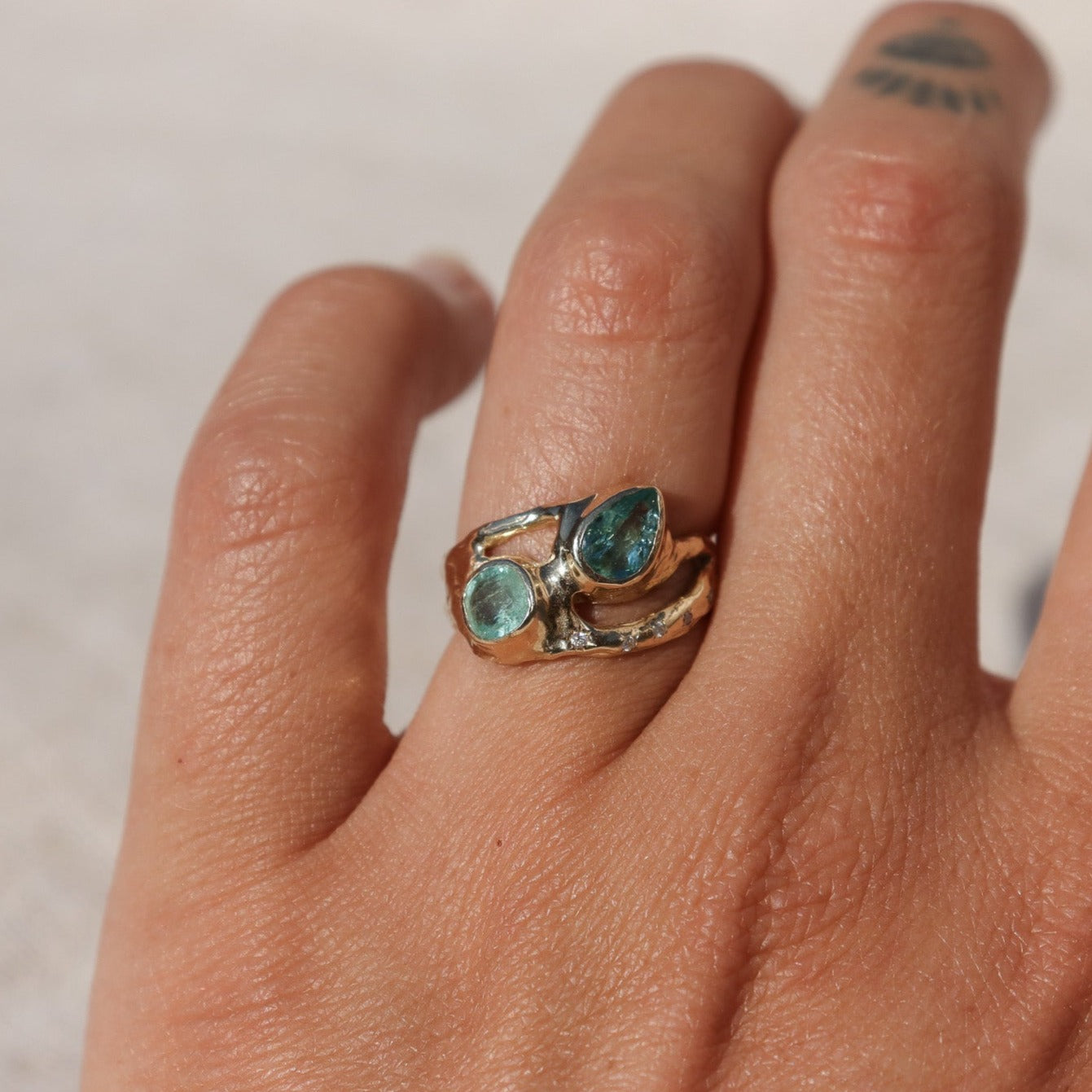 Exquisite ring featuring two vibrant Paraiba tourmalines elegantly bezel-set along a wide, organically shaped band, worn on a finger to depict scale.