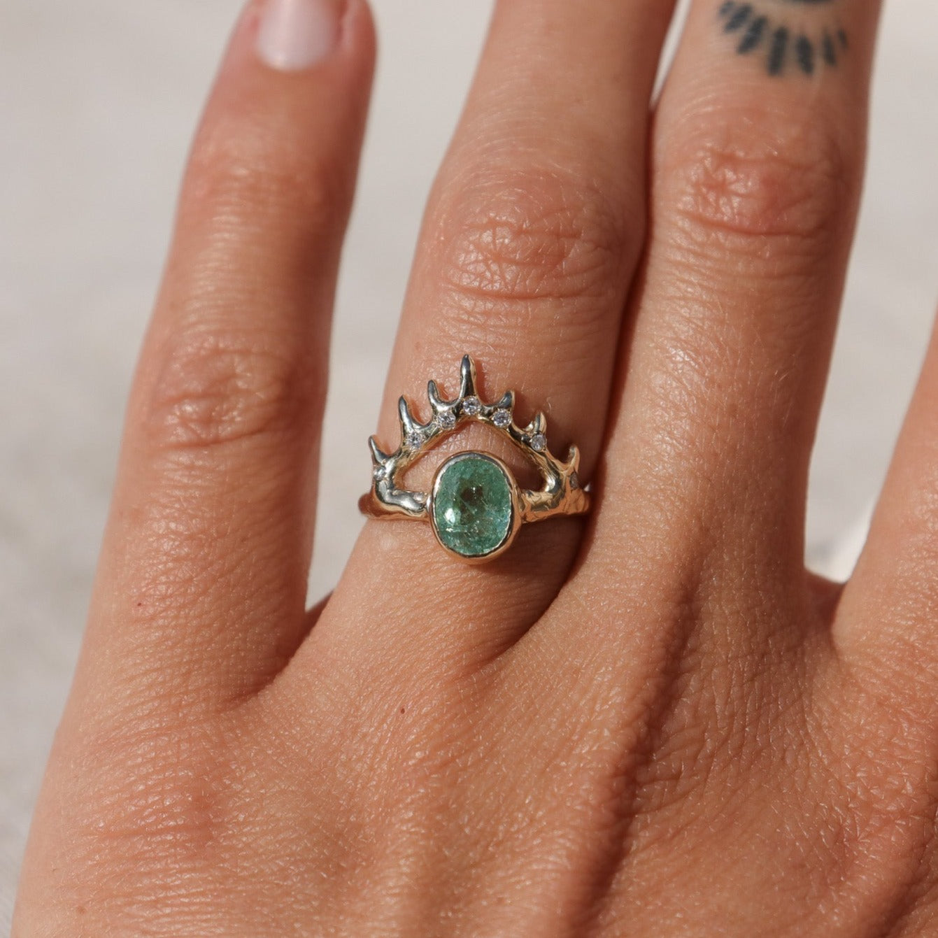 Elegant oval Paraiba tourmaline bezel-set in a coral-inspired crown-like V-shaped gold setting, accentuated by sparkling diamond details, worn on a finger to show scale.