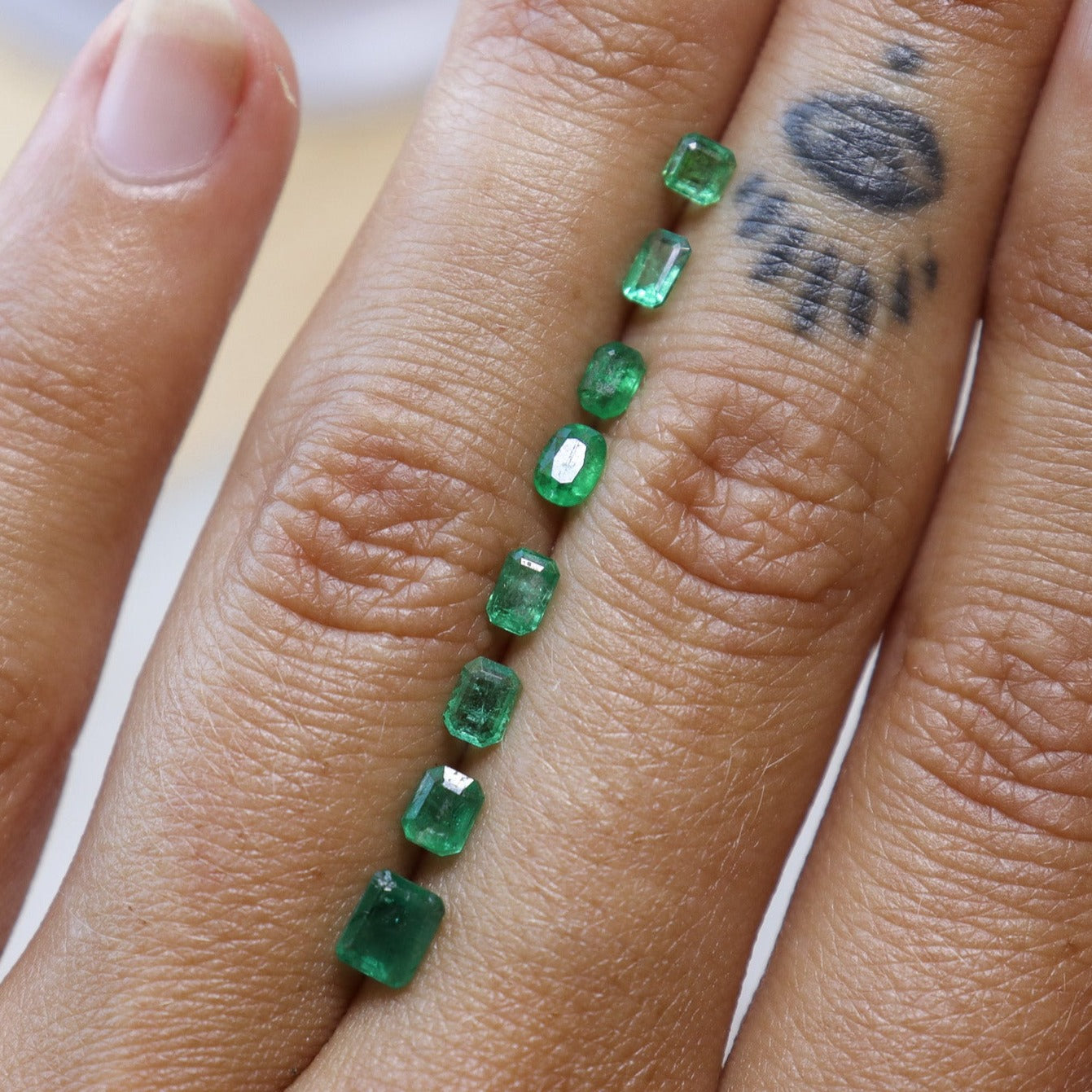 An array of emeralds shown on a hand for size and color comparison to choose from when creating your own ring.