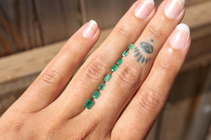 An array of emeralds shown  on a hand for  size and color comparison to choose from when creating your own ring.