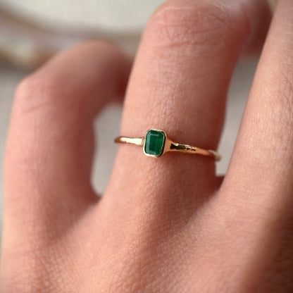 Mini emerald ring elegantly worn on a finger, showcasing its vibrant green gemstone and delicate gold band.