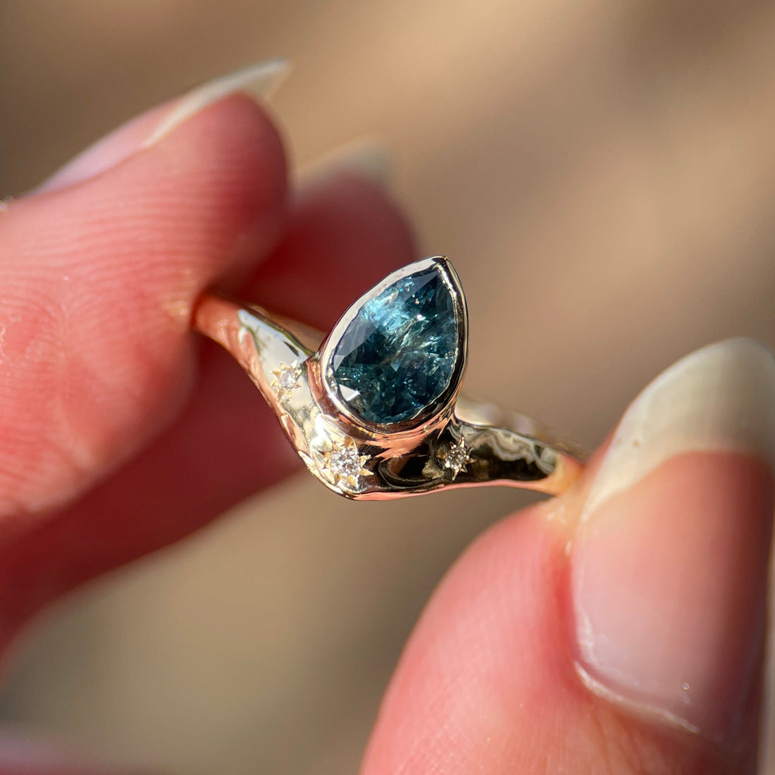 Gold ring with a blue gemstone held between fingers against a blurred natural background