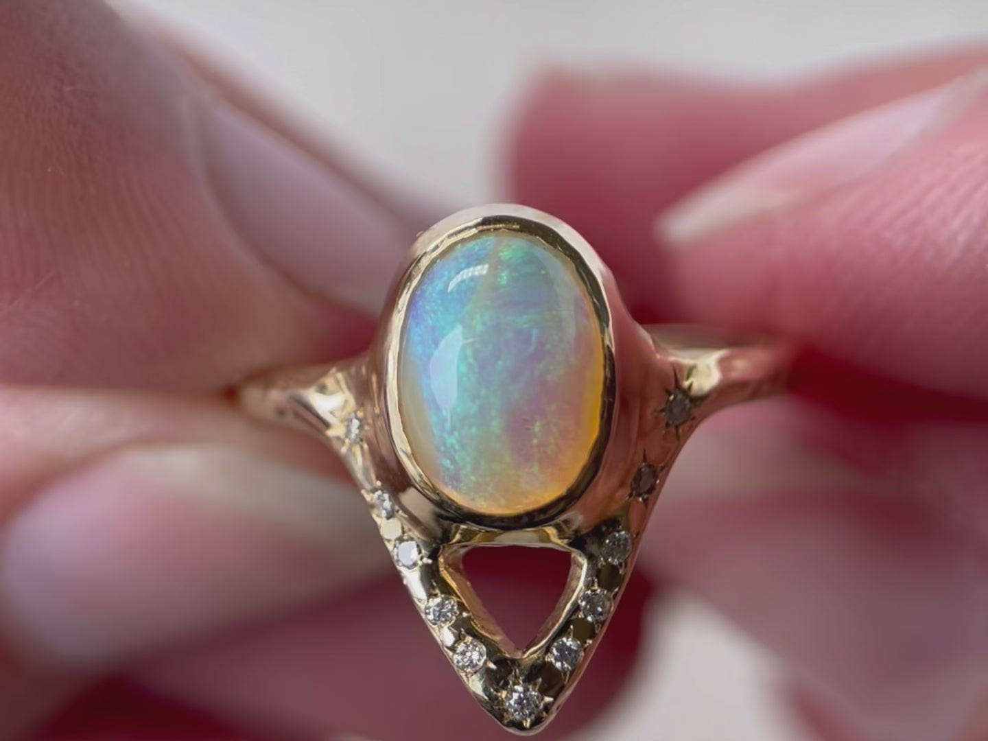 A close up video of an elegant opal ring featuring a V-shaped design adorned with sparkling diamond accents.