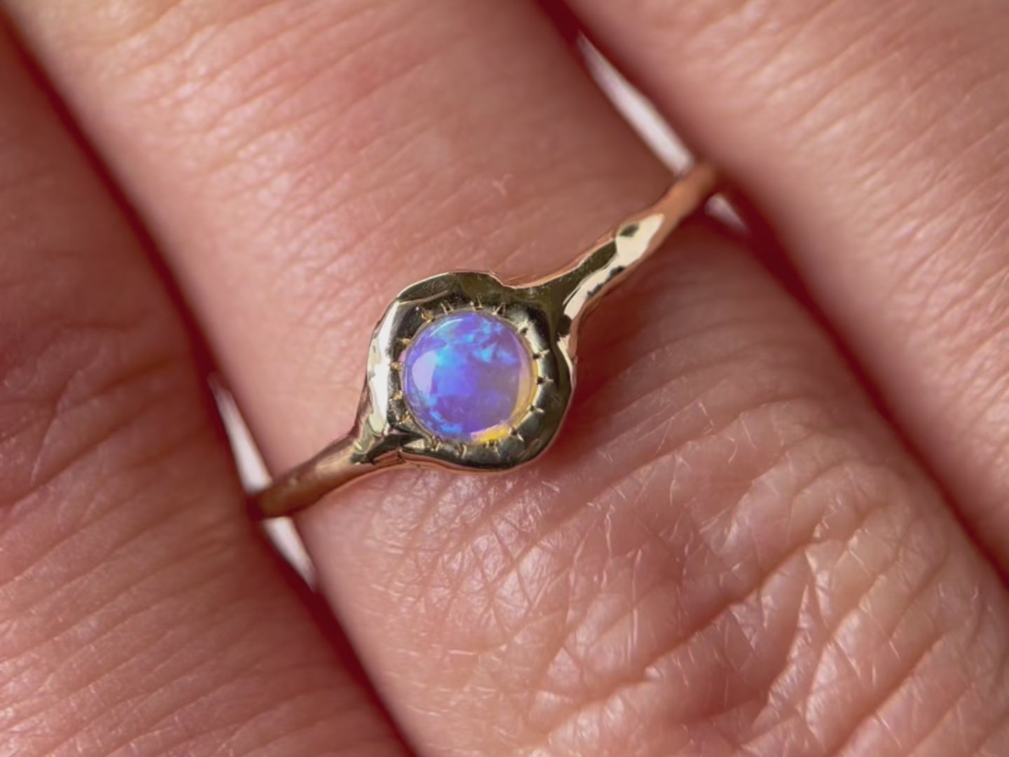 A close up video of a round opal ring, set on a slender band with small tick-like accents that radiate like a starburst, creating a mesmerizing and celestial jewelry piece.