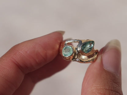 A close up video of an exquisite ring featuring two vibrant Paraiba tourmalines elegantly bezel-set along a wide, organically shaped band