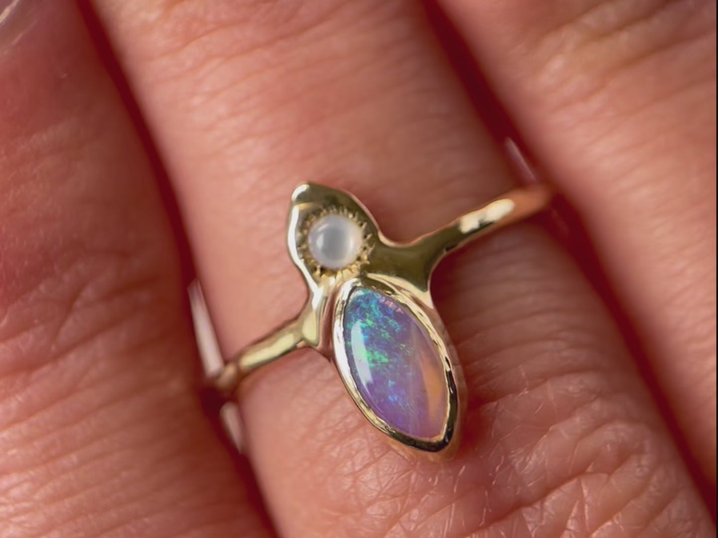 A close up video of the 'Tidal Treasure' ring design featuring a vertically-set marquise-cut opal at its center, with a round mother of pearl cabochon positioned above it. Delicate ticks radiate from the opal, resembling a mesmerizing starburst.