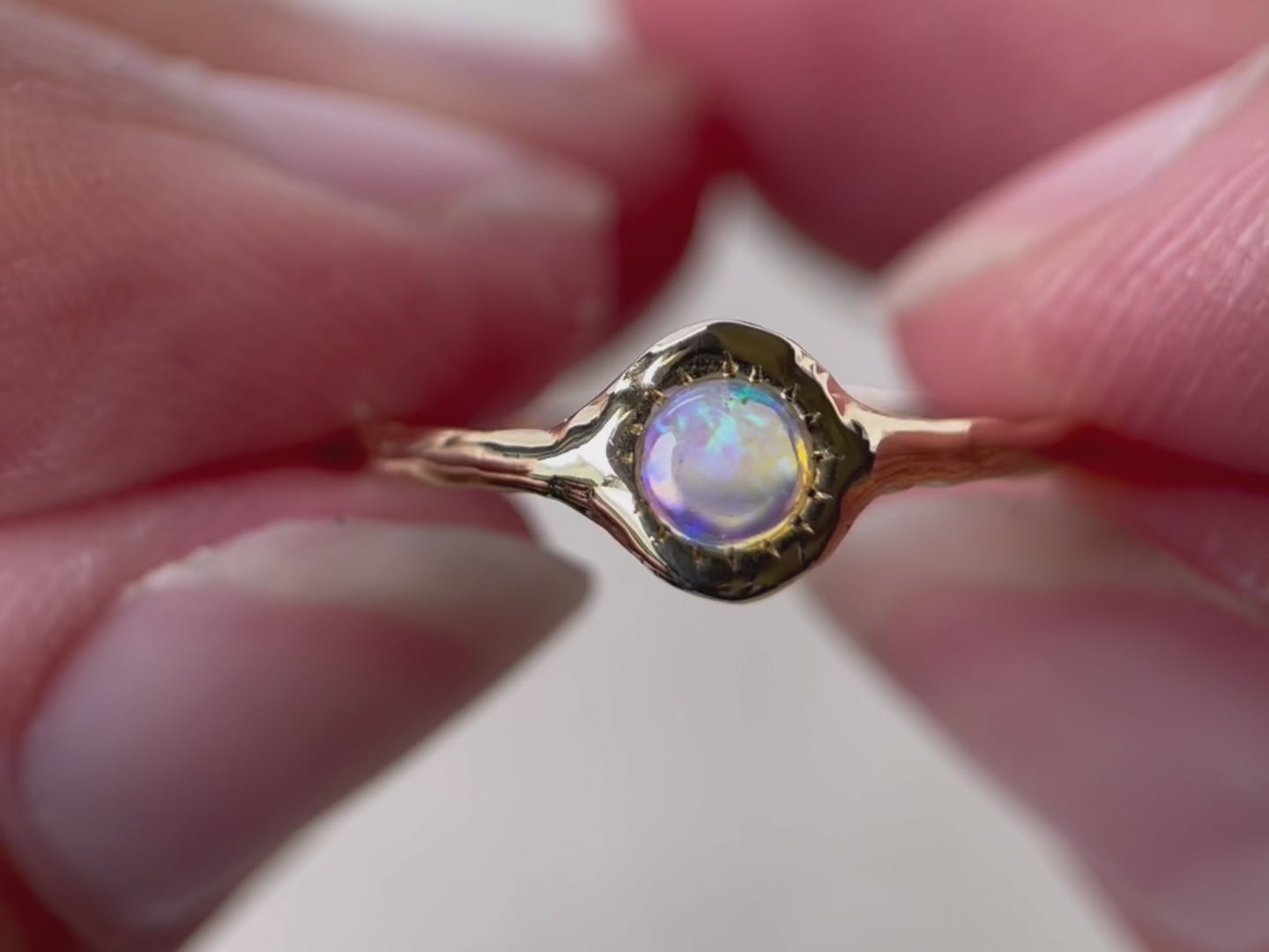 A close up video of a round opal ring, set on a slender band with small tick-like accents that radiate like a starburst, creating a mesmerizing and celestial jewelry piece.