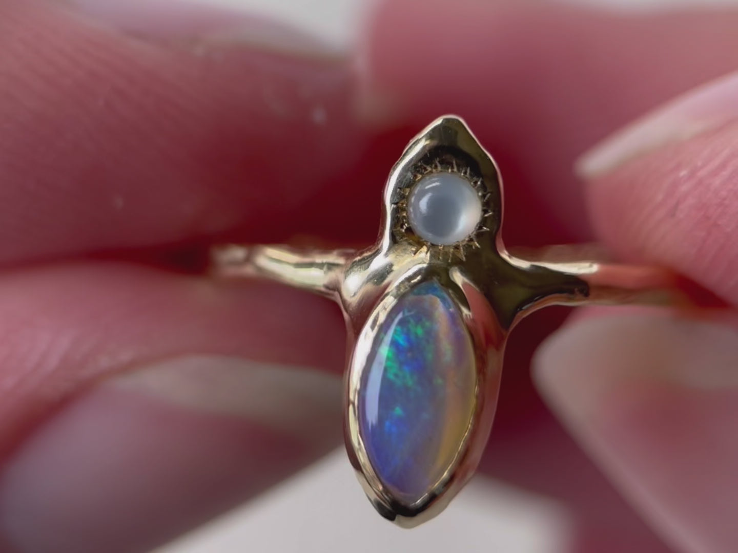 A close up video of the 'Tidal Treasure' ring design featuring a vertically-set marquise-cut opal at its center, with a round mother of pearl cabochon positioned above it. Delicate ticks radiate from the opal, resembling a mesmerizing starburst.