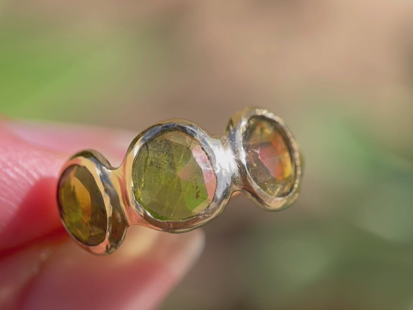 A close up video of three rose  cut green tourmaline stones are bezel  set in 14k gold along an organic band.