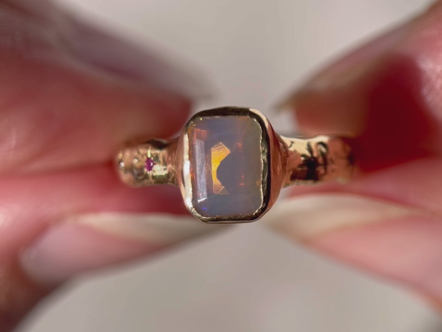 A close up  video of an emerald cut opal is bezel  set  in 14k  gold  with a wide  band that  features  ombre sapphires  star  set a long  each side of the band.