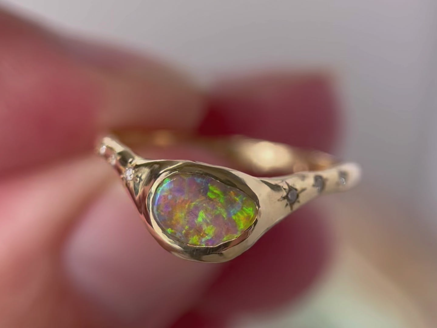 Close up video of a  crystal boulder opal that is bezel set on an  organically crafted band with three star set diamonds on each side of the stone.