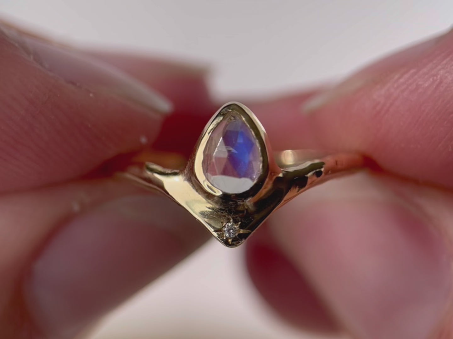 A close up video of a pear-shaped moonstone, bezel-set with a dazzling diamond star positioned at the base for a celestial-inspired and enchanting jewelry design.