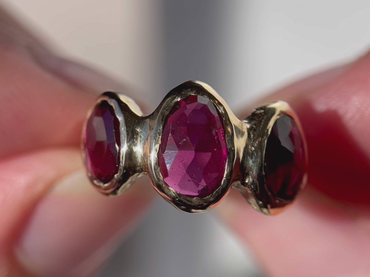 Close  up of three rose cut rhodolite garnets that are bezel set  on an organically crafted 14k gold band.