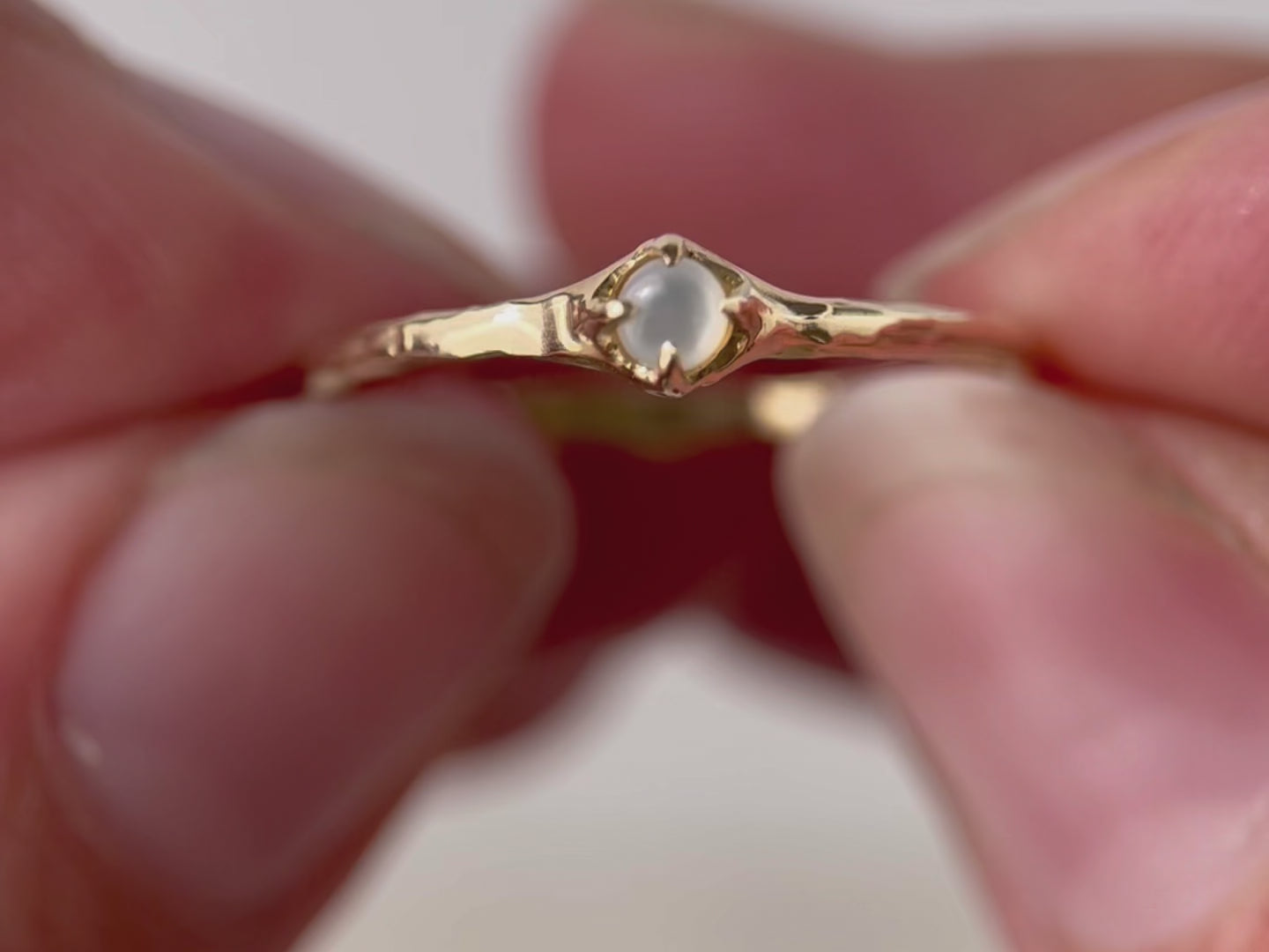 A close up video of a tiny mother of pearl cabochon delicately prong-set on a dainty band, creating an understated and elegant jewelry piece.