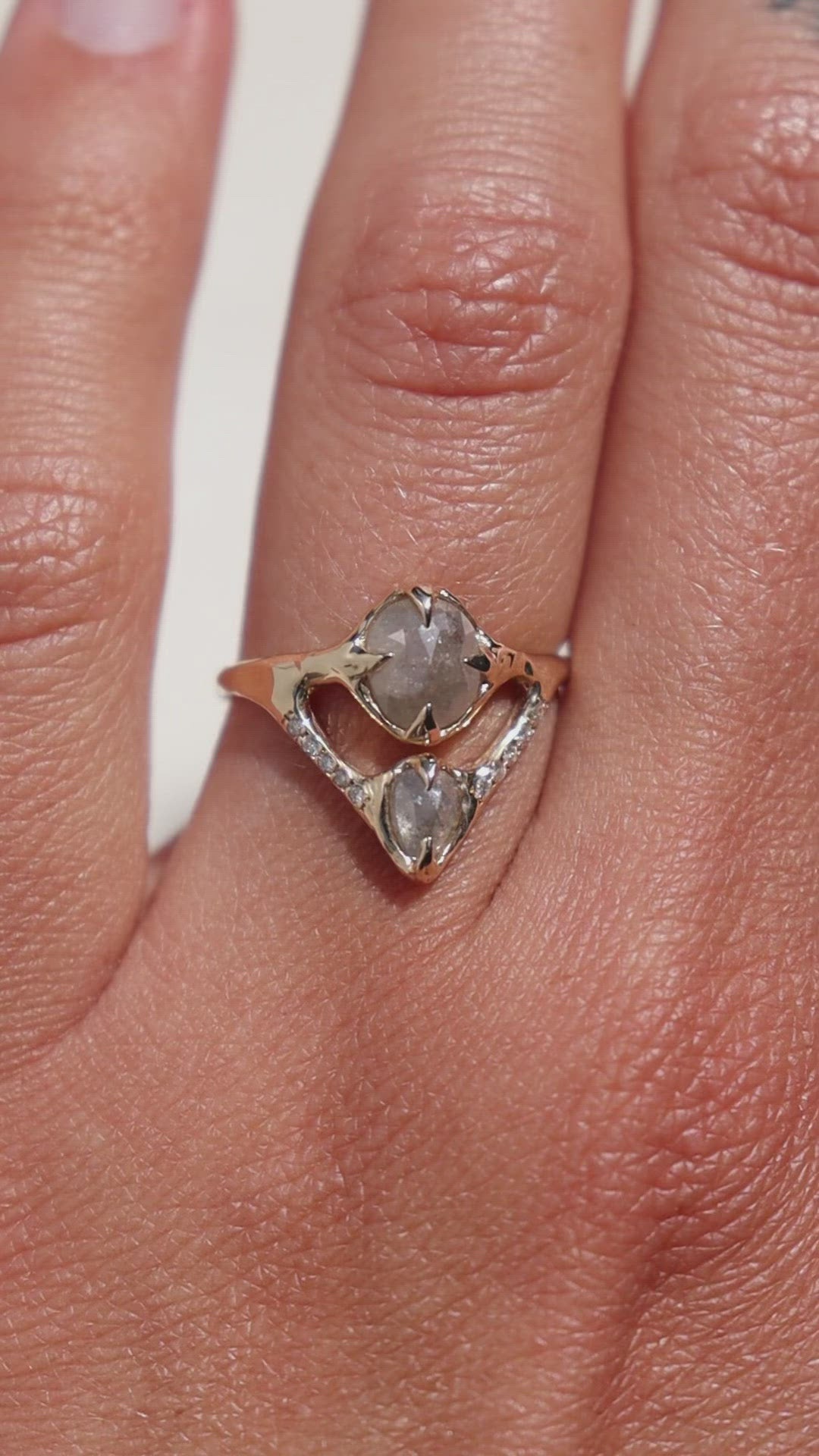 video close up of a gold rustic diamond ring, there are two gray diamonds prong set and a v-shaped row of pave diamonds
