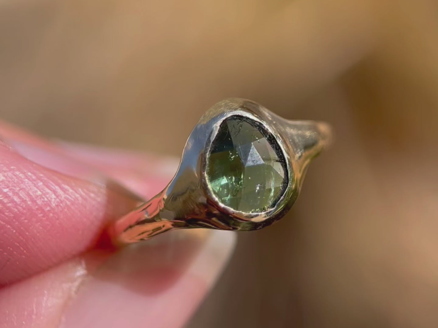A close up  video of a rose cut blue green tourmaline is set in 14k  gold  into a signet style ring.
