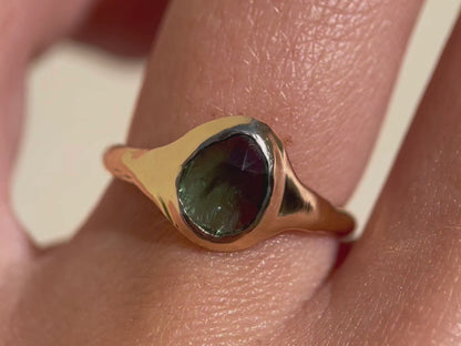 A close up video of a rose cut blue green tourmaline is set in 14k  gold  into a signet style ring.