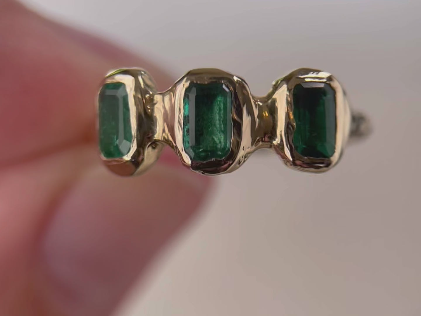 Close  up  video  of  three small emerald cut emeralds that are embedded into a 14k gold ring giving it an organic look.