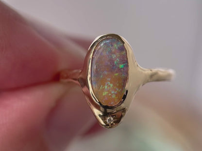 A close up video of a long oval opal that is bezel set in 14k gold  with  a star set  diamond at the base of the ring.