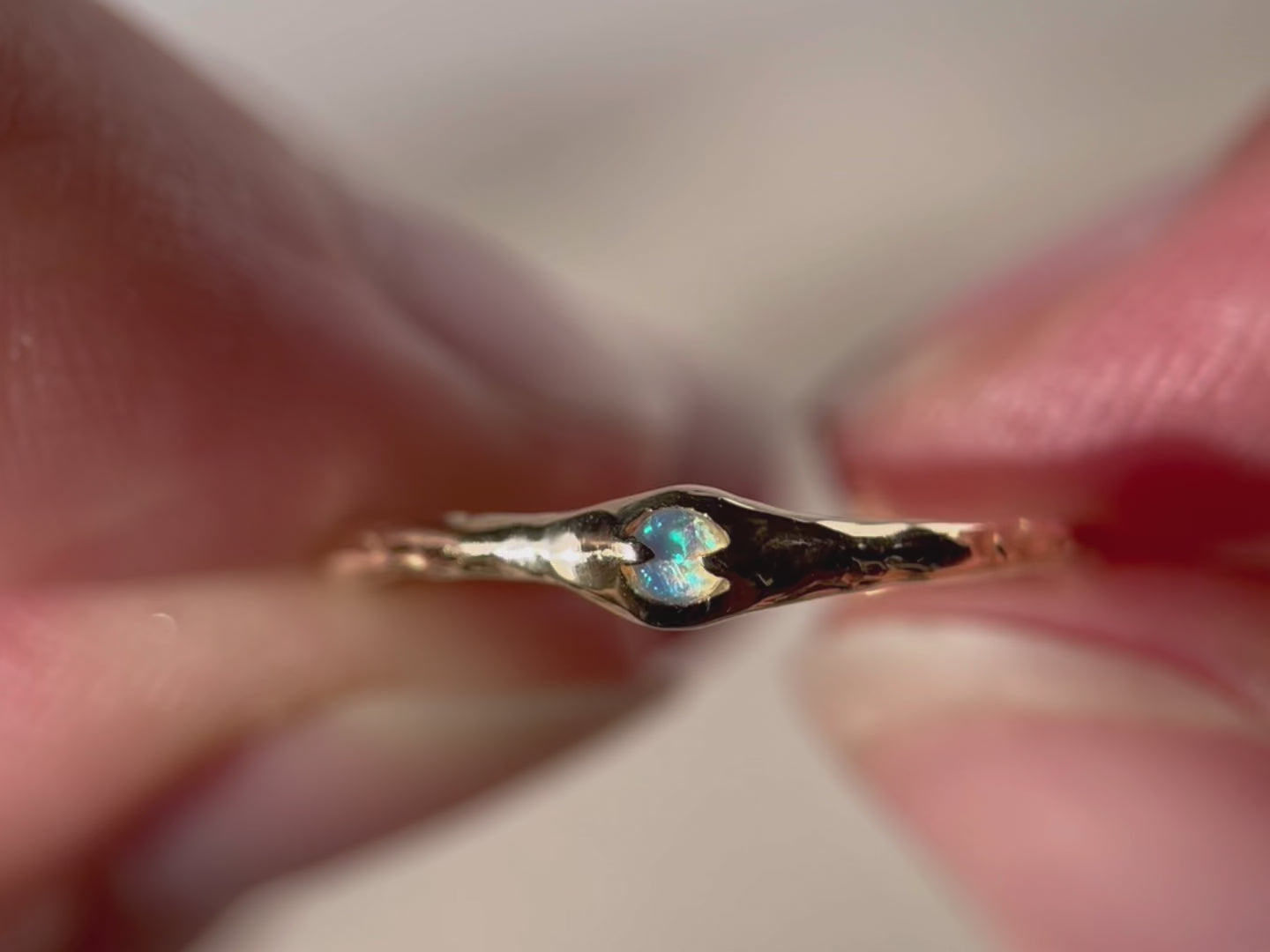 A  close up of a tiny opal that is prong set on a narrow 14k gold band.