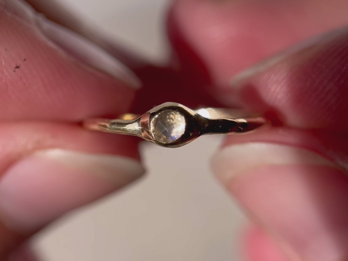 Close up video of a rose cut moonstone bezel set in 14k gold on a narrow band.
