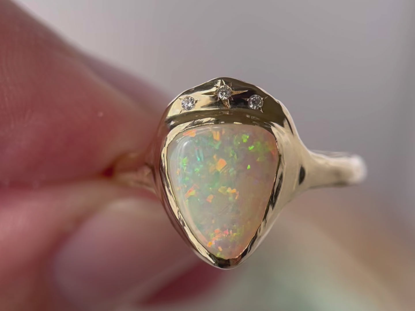 Close up video of a White triangle opal is bezel set in 14k gold with three star set diamonds.