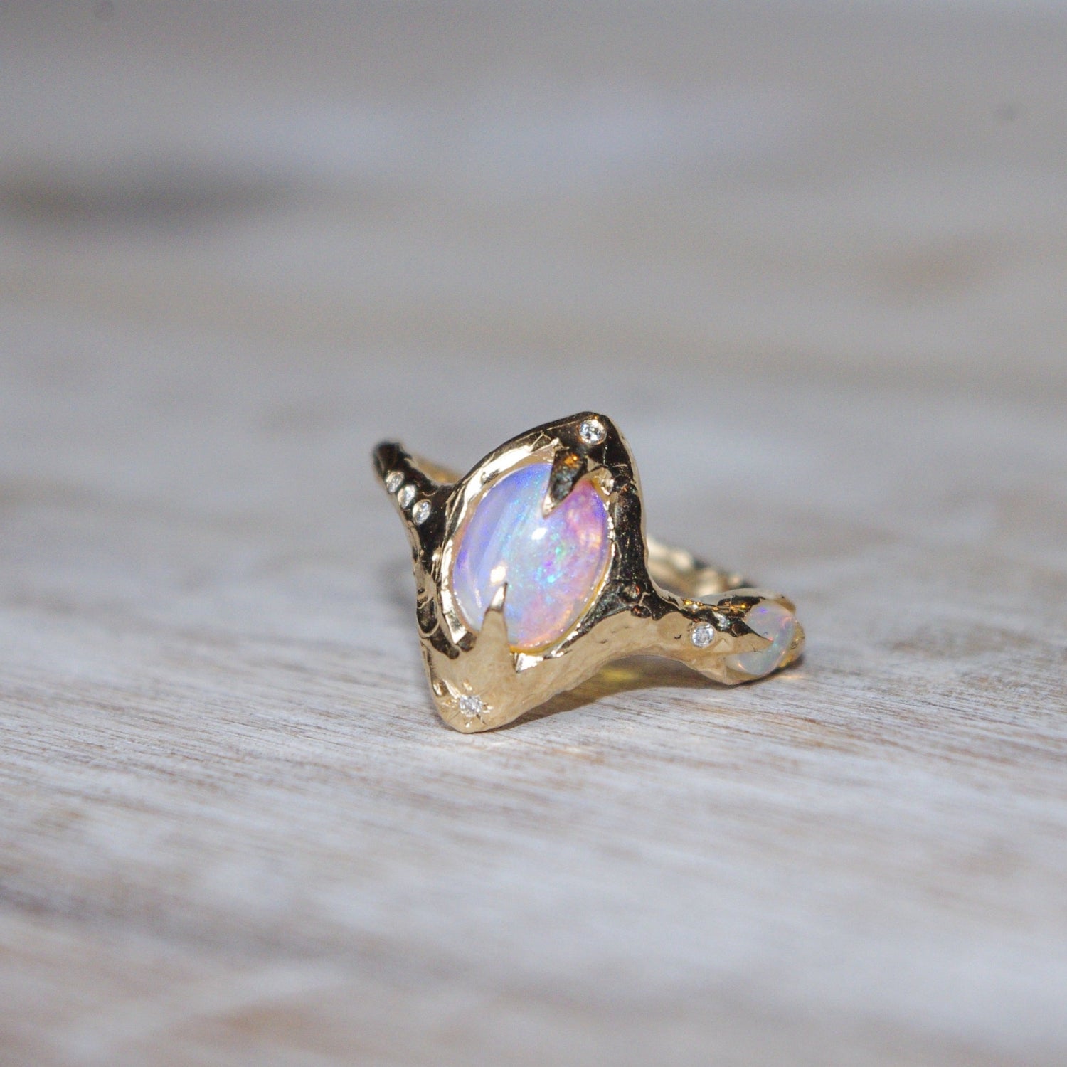 a blue and pink colored pipe opal is prong set in gold and surrounded by diamonds