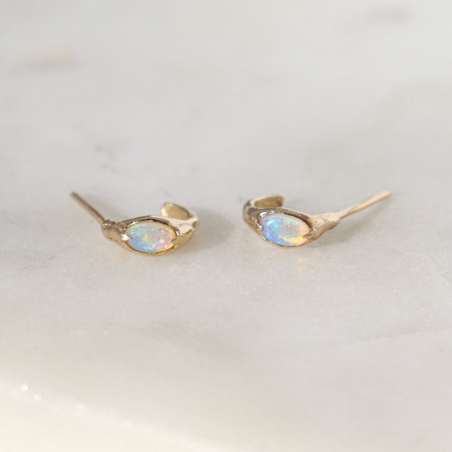 A pair of opal huggie hoops laid on their side on a white surface