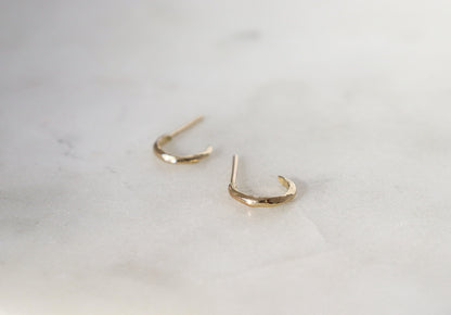 A pair of plain huggie hoops laid out flat on their sides on a white surface