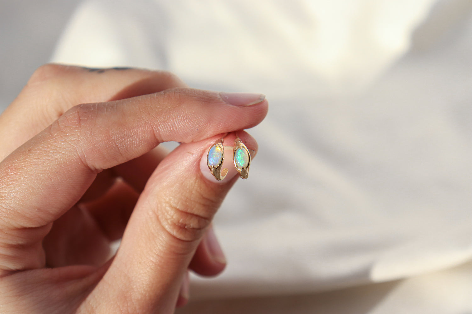 Hand holding a pair of opal huggie hoops to show size