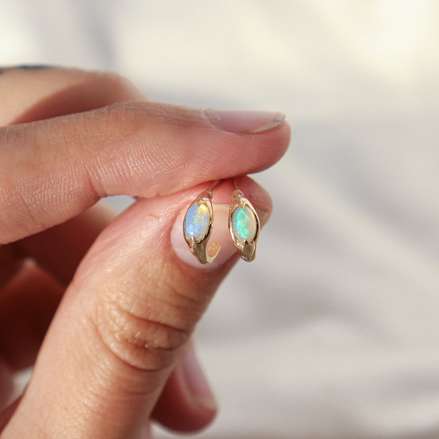 Hand holding a pair of opal huggie hoops to show size