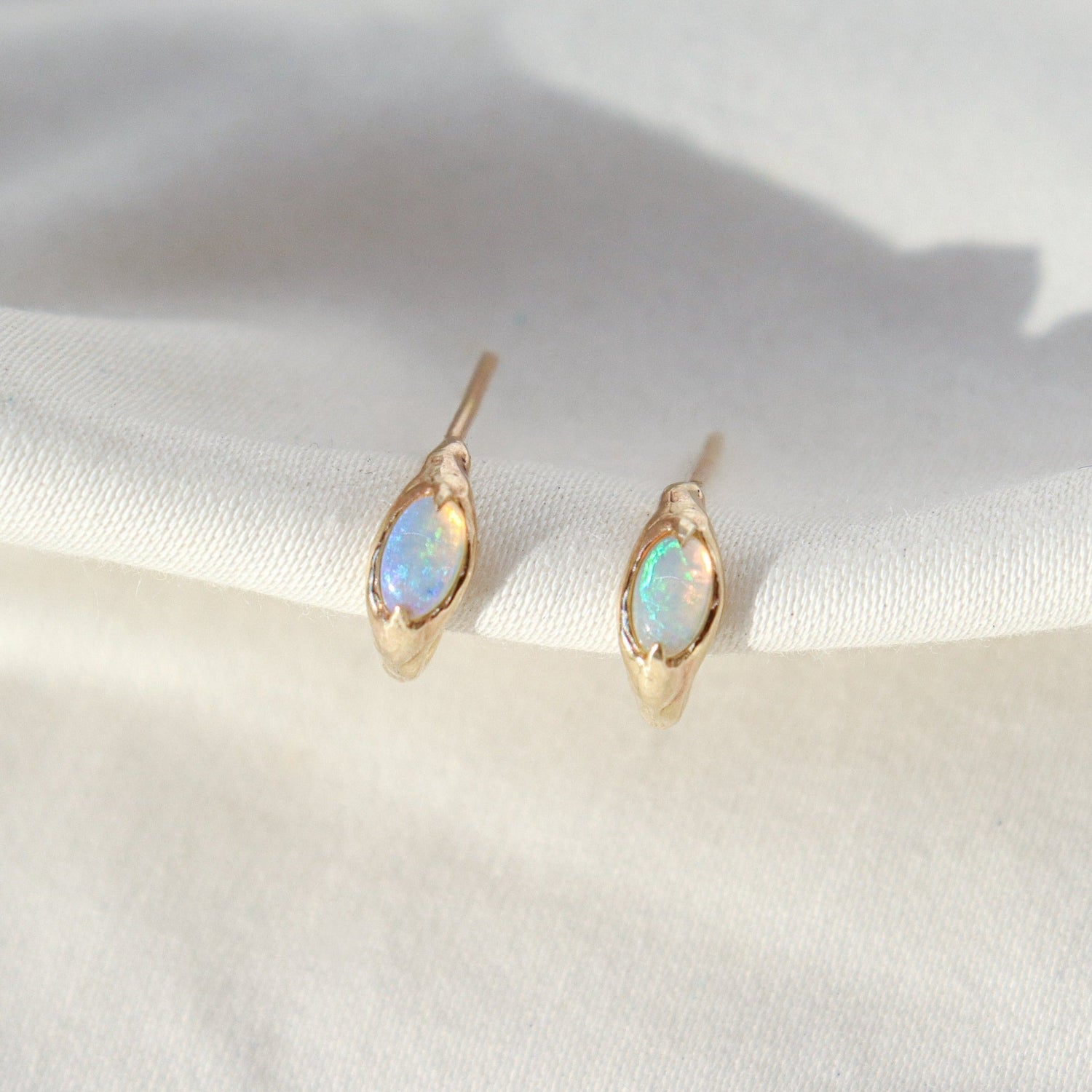 Tiny opal huggie hoops are positioned on a white background