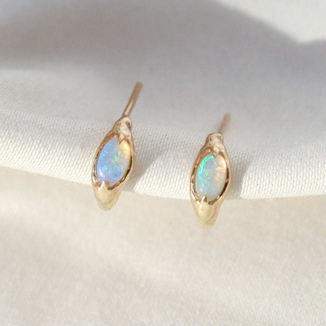 Tiny opal huggie hoops are positioned on a white background