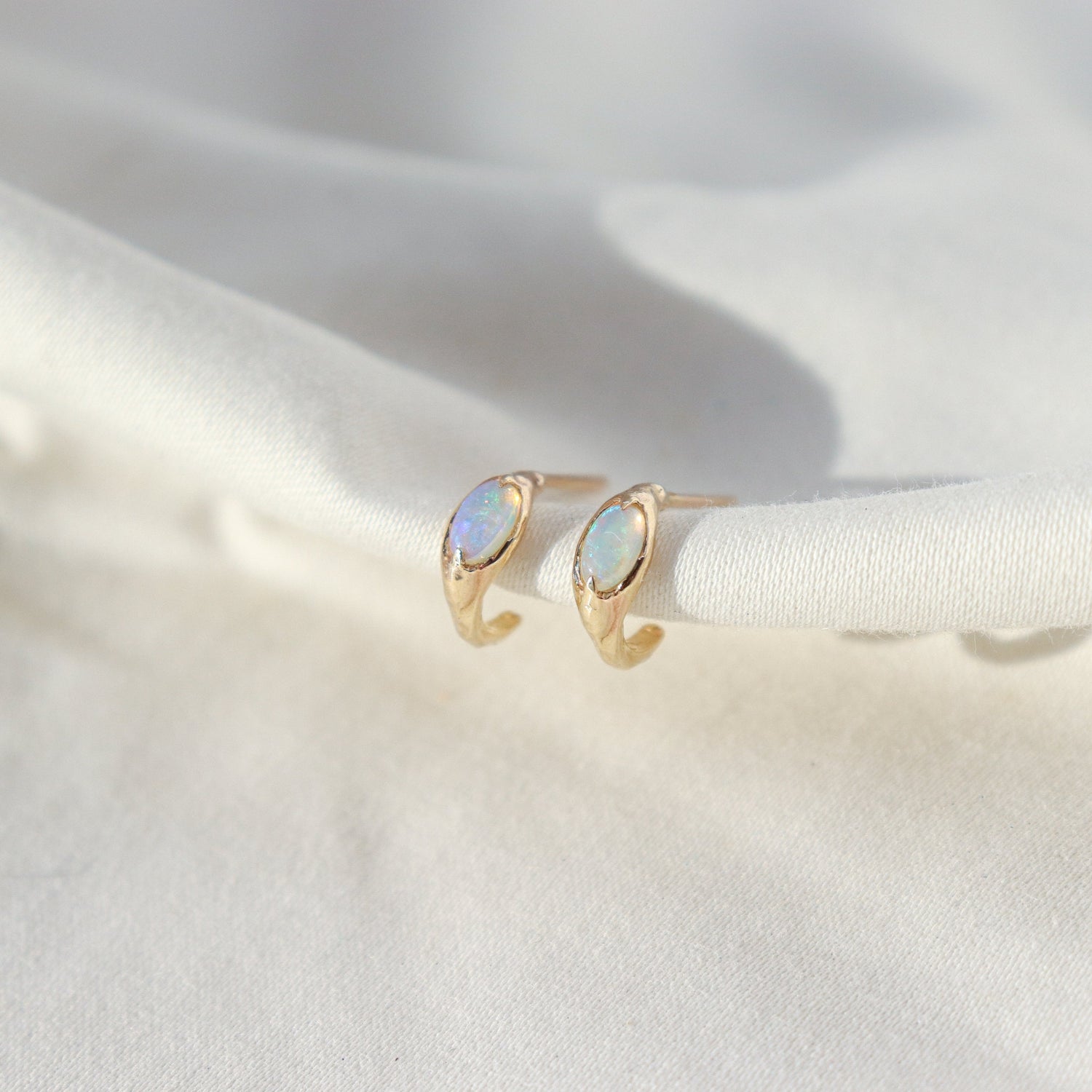 Side view of opal huggie hoops on a white background