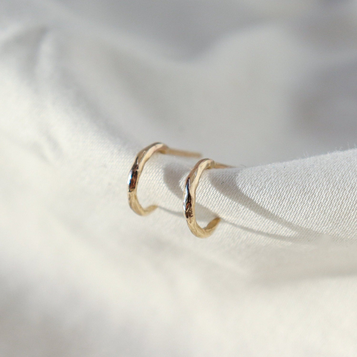 A pair of classic huggie hoops positioned on white fabric