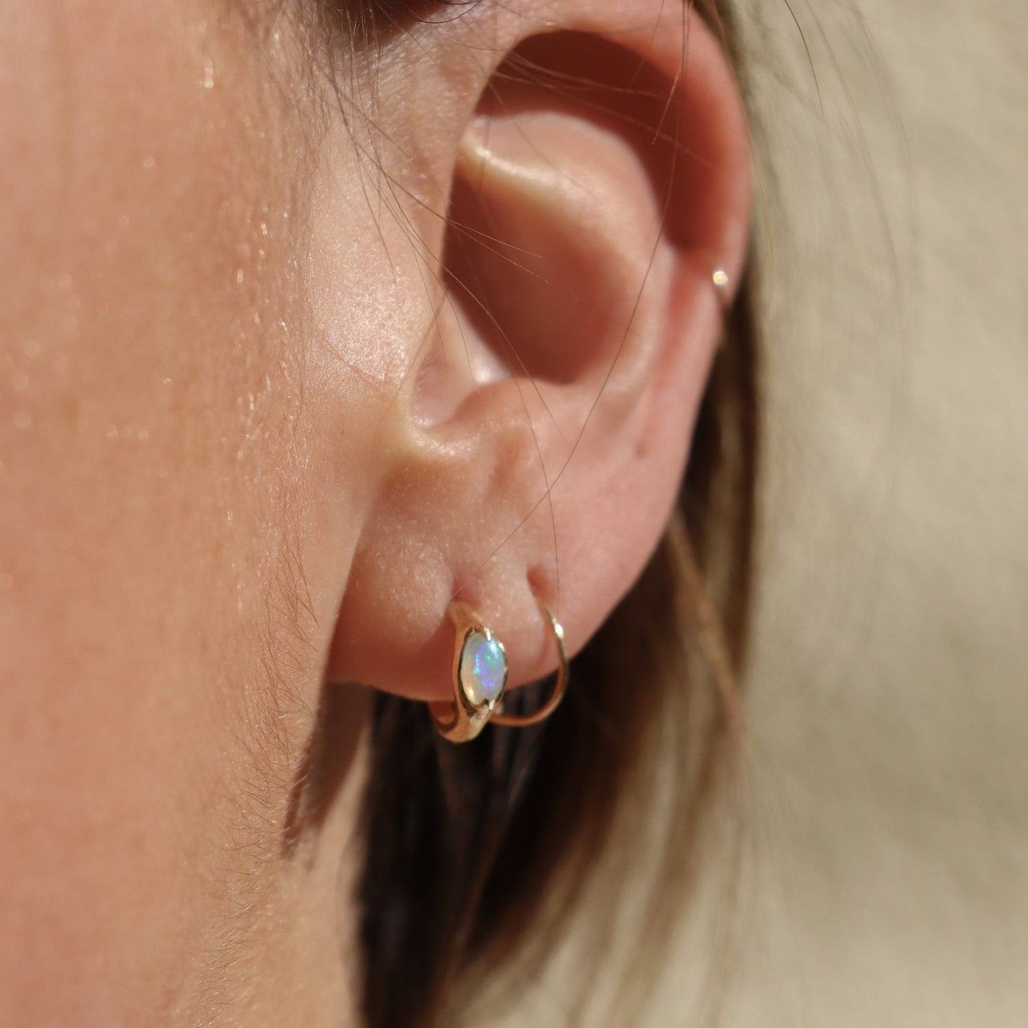 Ear wearing opal huggie hoops to show size