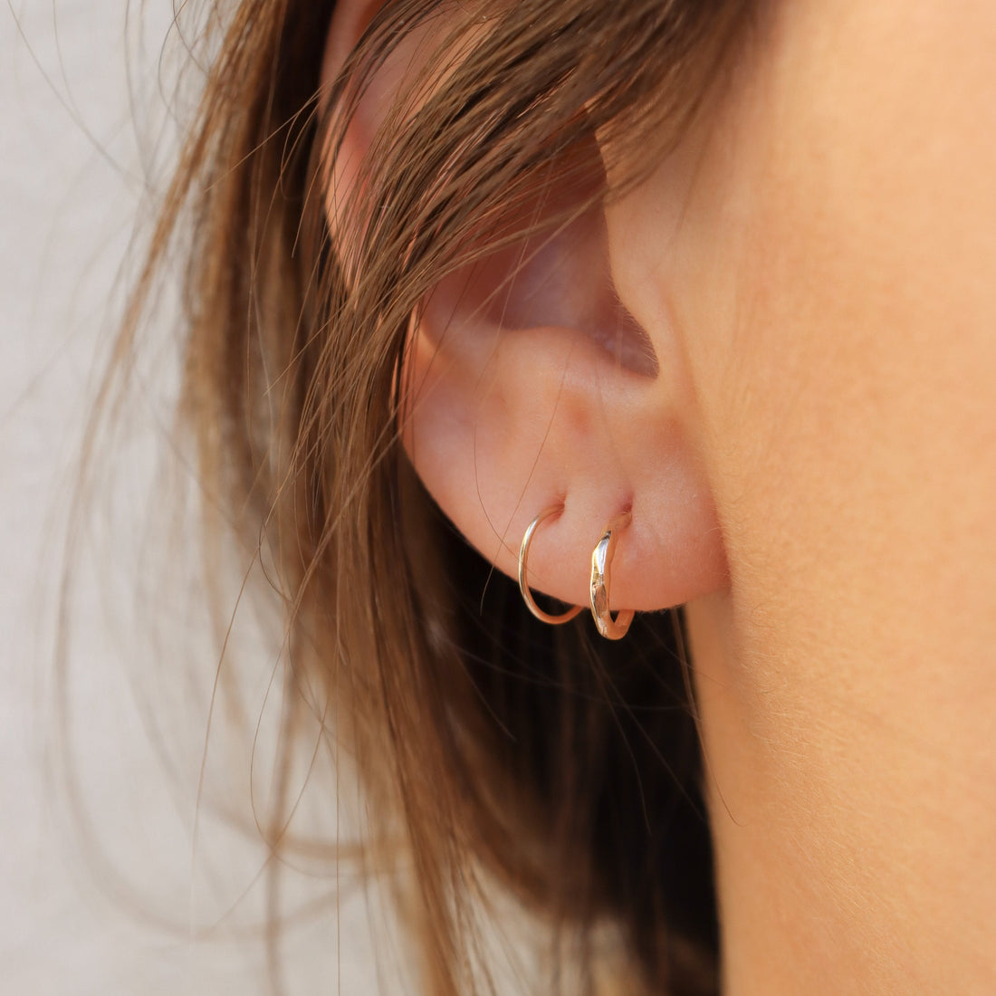 An ear wearing two different hoops to show the thickness of each side by side