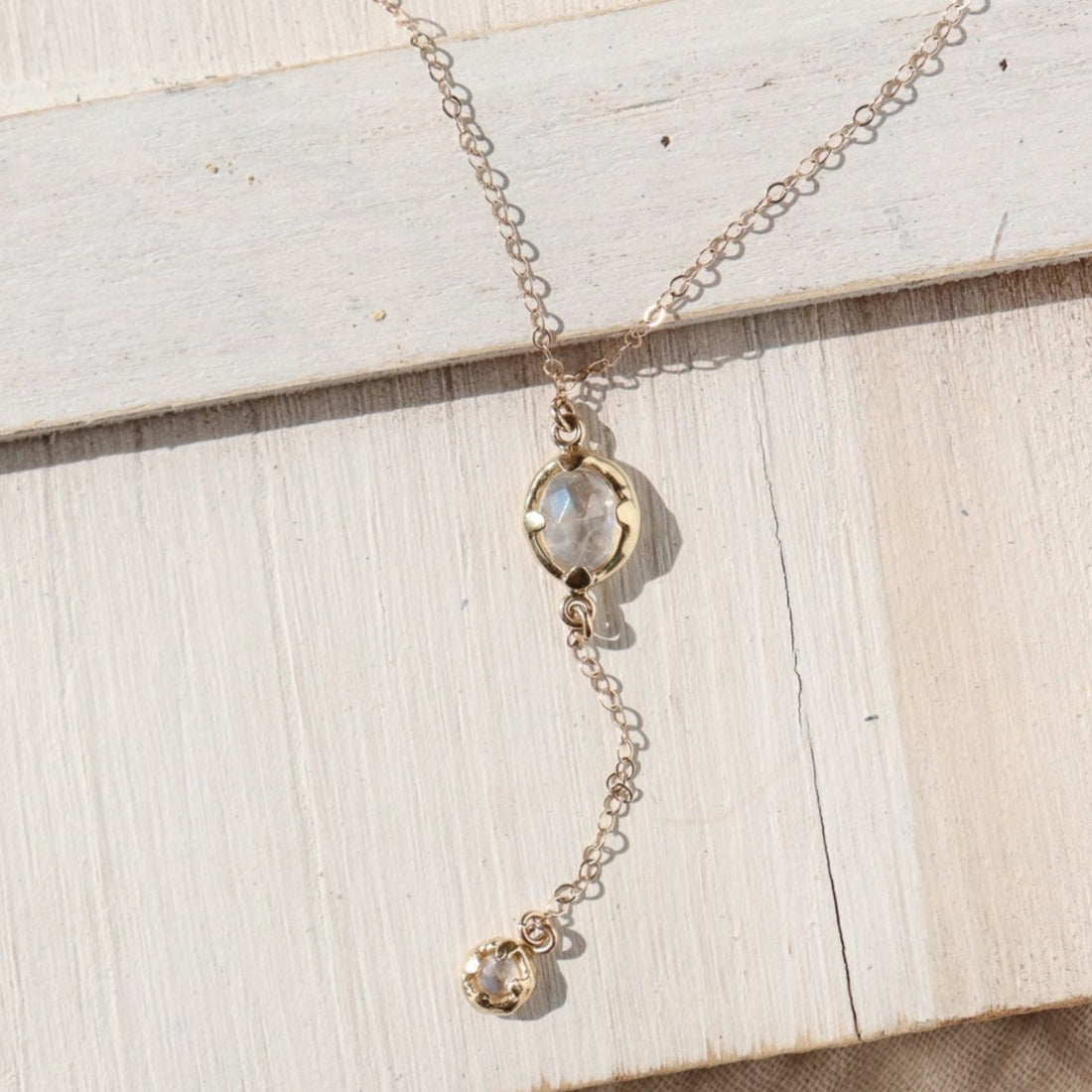 A rainbow moonstone lariat necklace lays on a white washed board