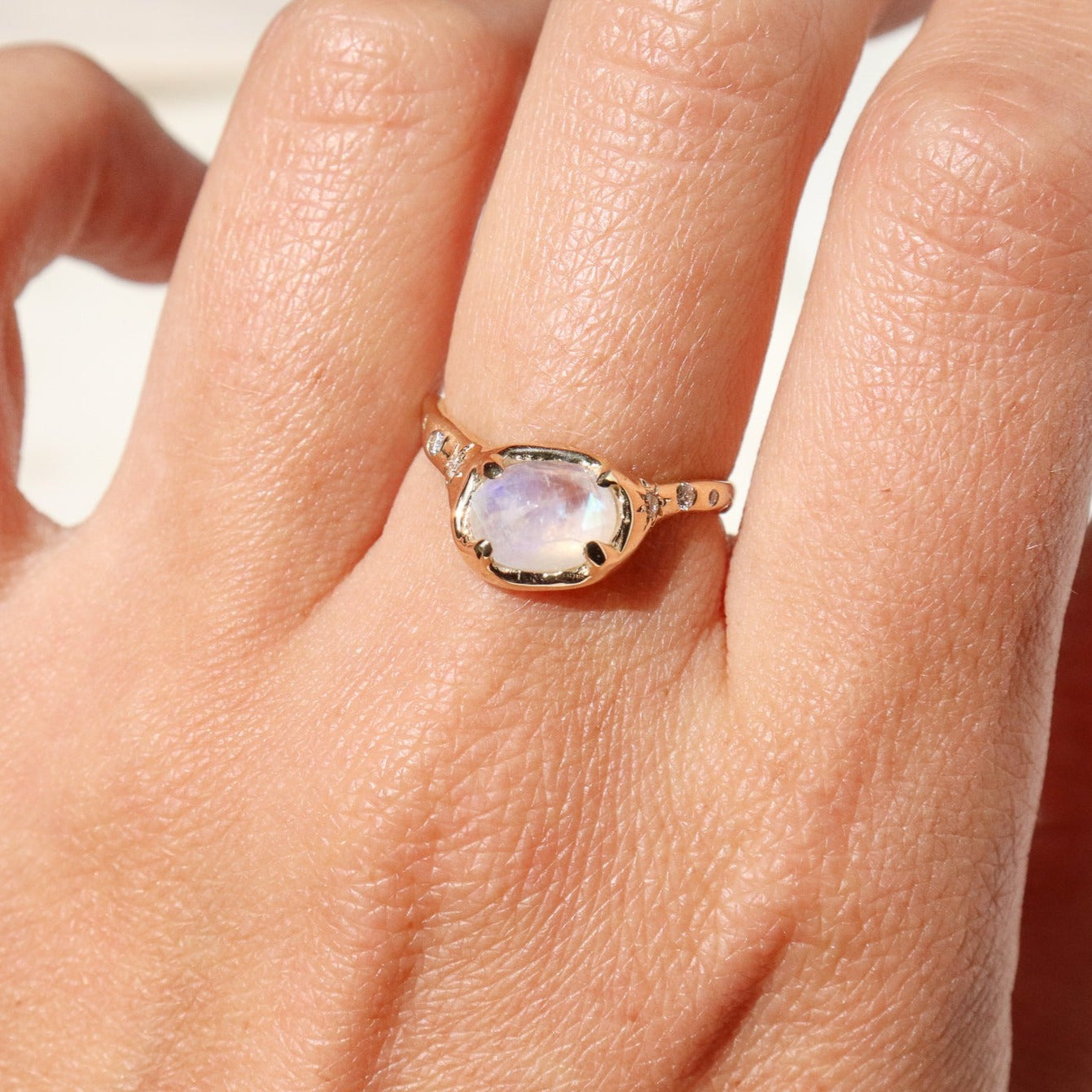 gold moonstone ring with diamonds is shown on a finger 