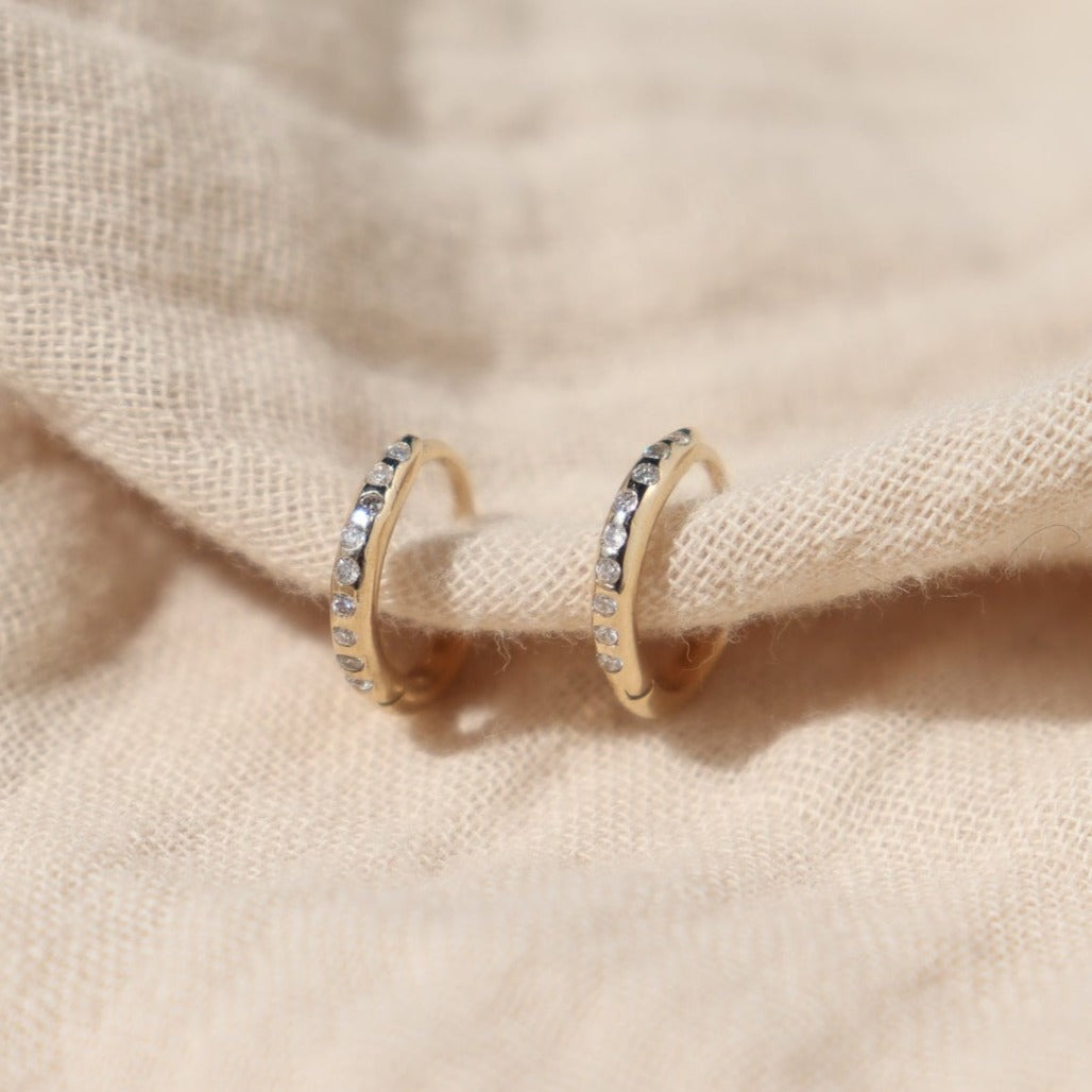 a pair of flush set diamond gold hoops are shown on a cream cloth