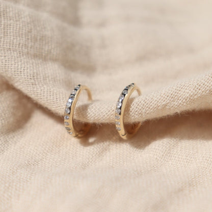 a pair of flush set diamond gold hoops are shown on a cream cloth