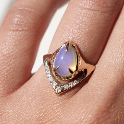 pear shaped pipe opal is prong set in a gold ring with a v-shaped band under the stone covered in pave diamonds
