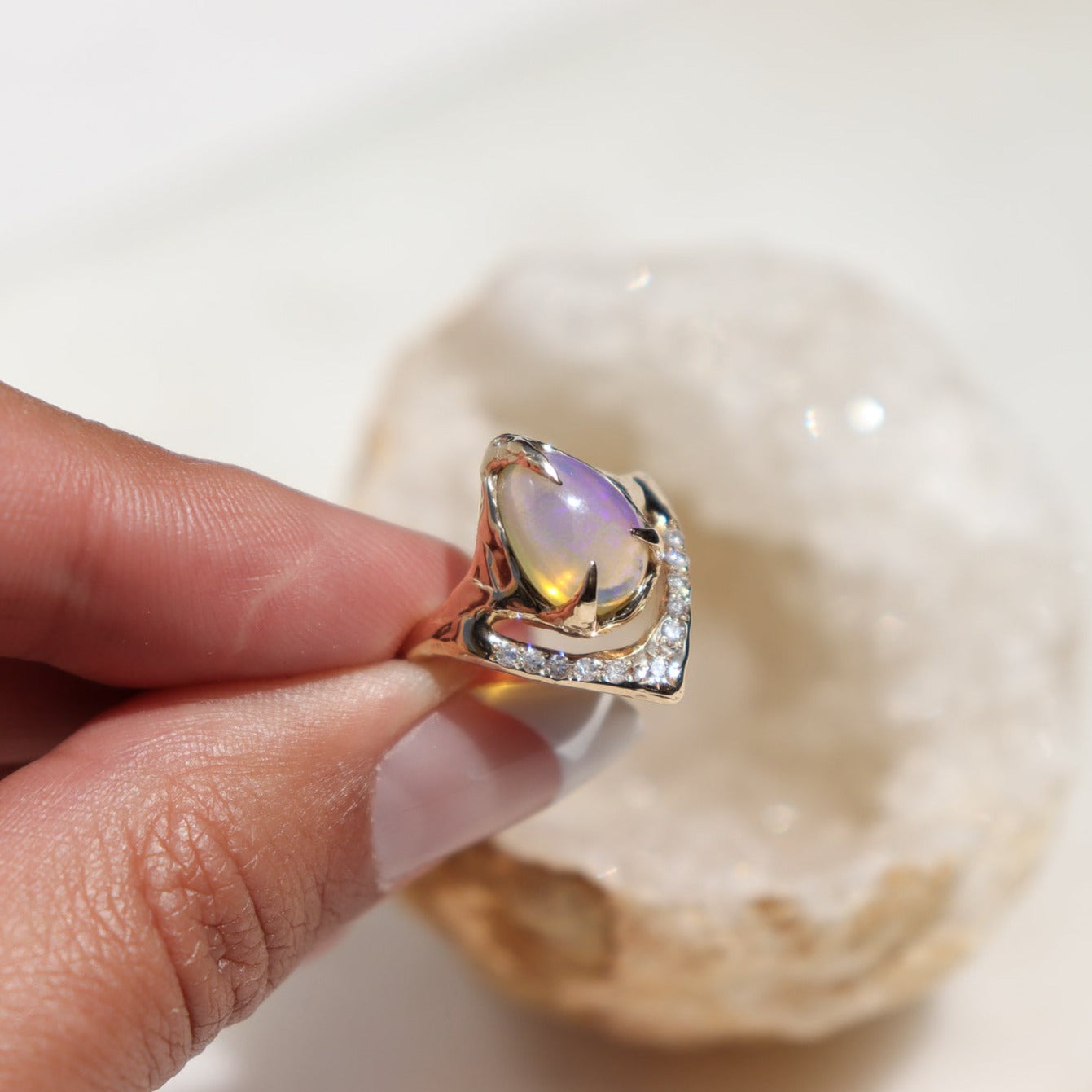 pear shaped pipe opal ring with pave diamonds is being held to show a 3/4 view