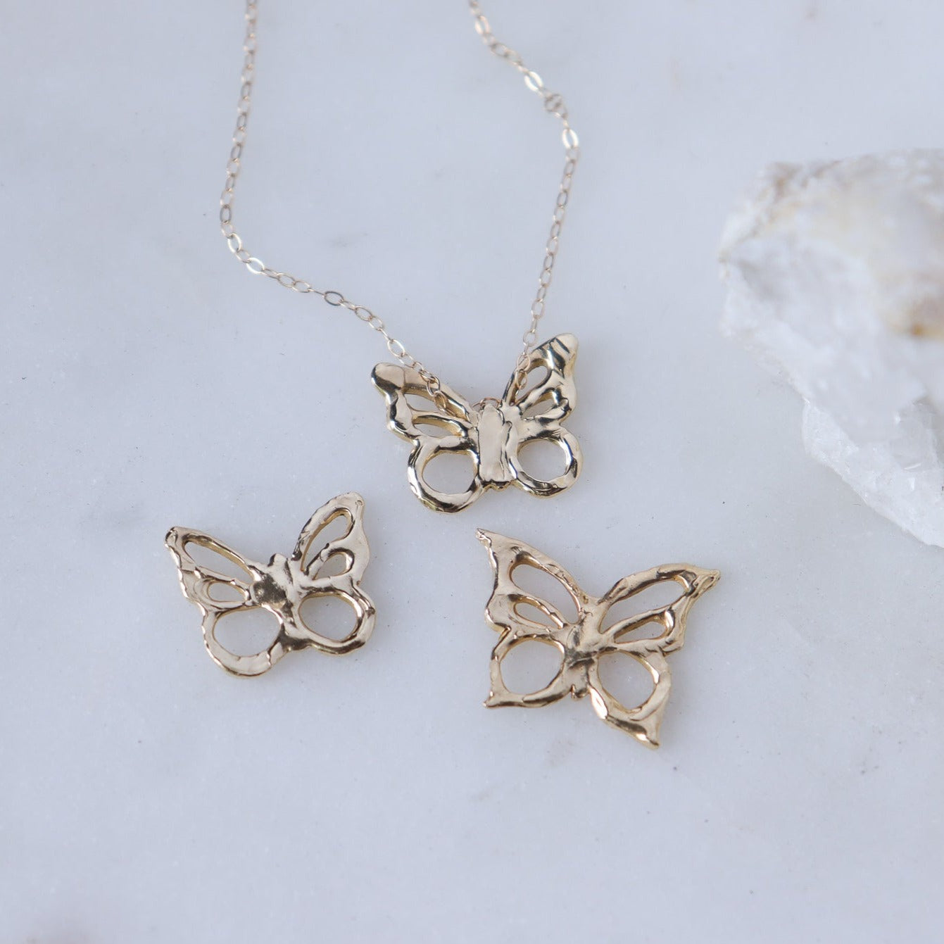 An array of 14k gold butterfly charms with one of the charms shown worn as a necklace.