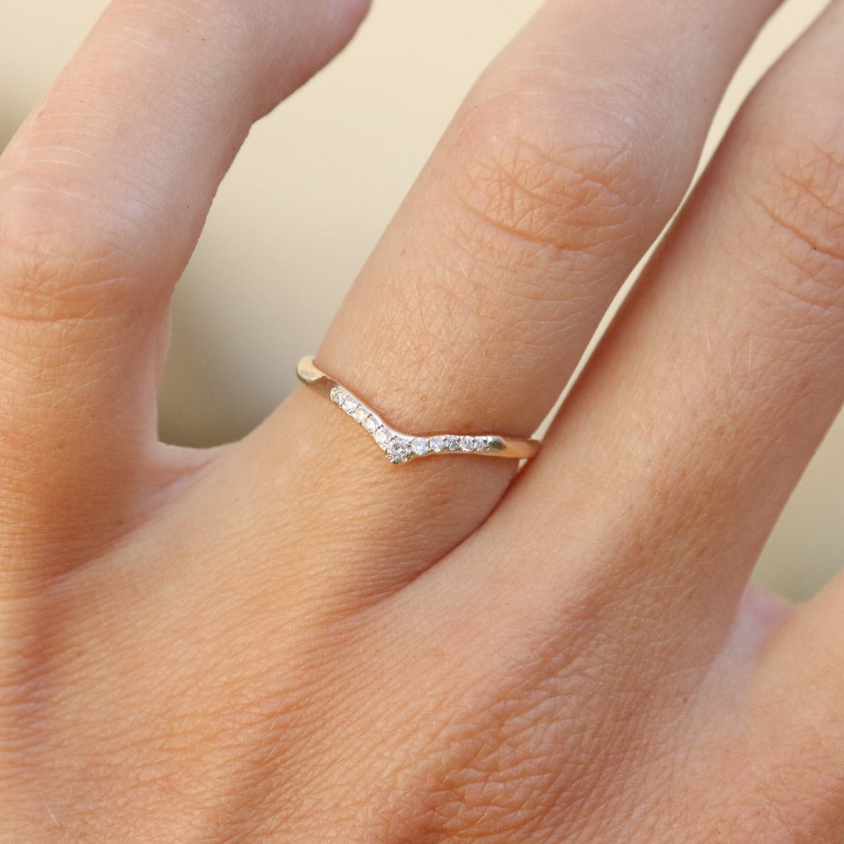 A pave diamond curved stacking band in 14k yellow gold is worn on a ring finger.