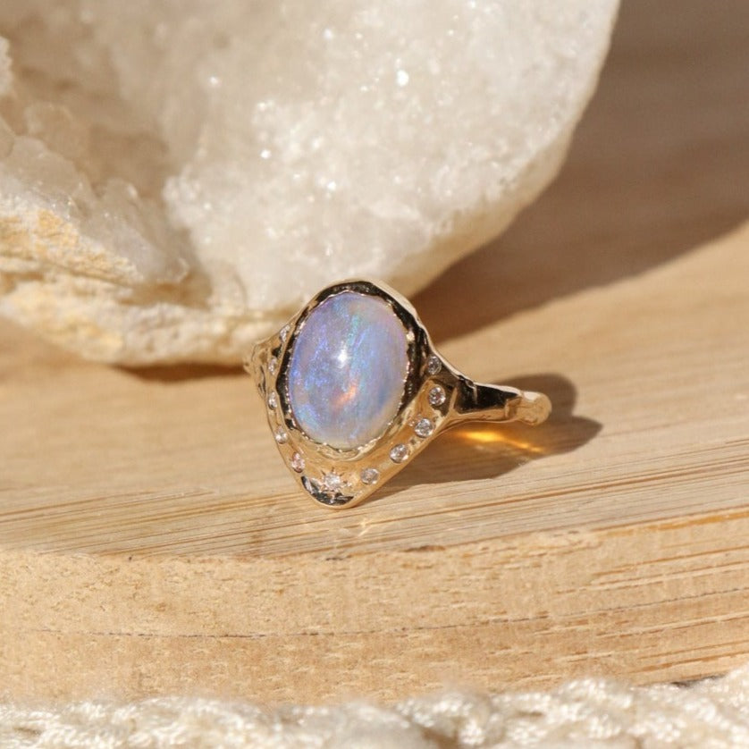 opal ring set in 14k gold with diamonds is displayed on a wooden surface