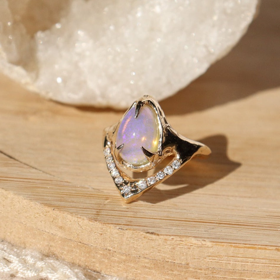 a pear shaped opal ring is prong set in 14k gold with pave diamonds