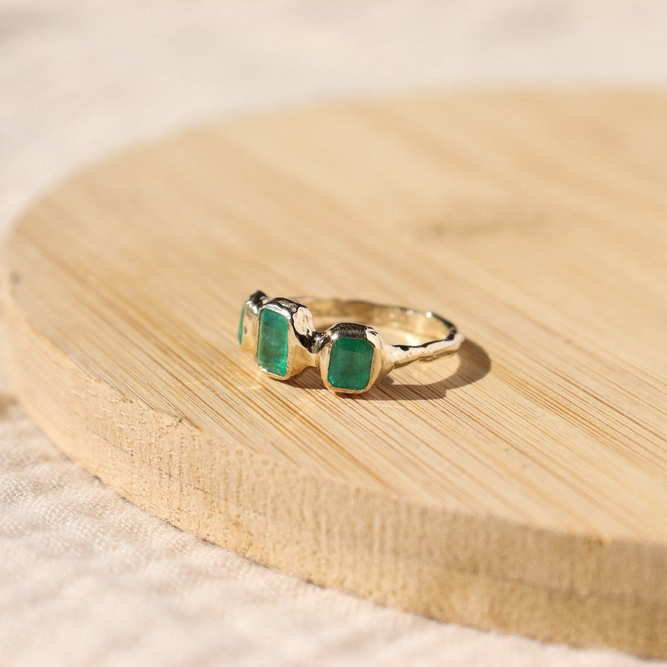 side view of a trio emerald ring positioned on a wood surface
